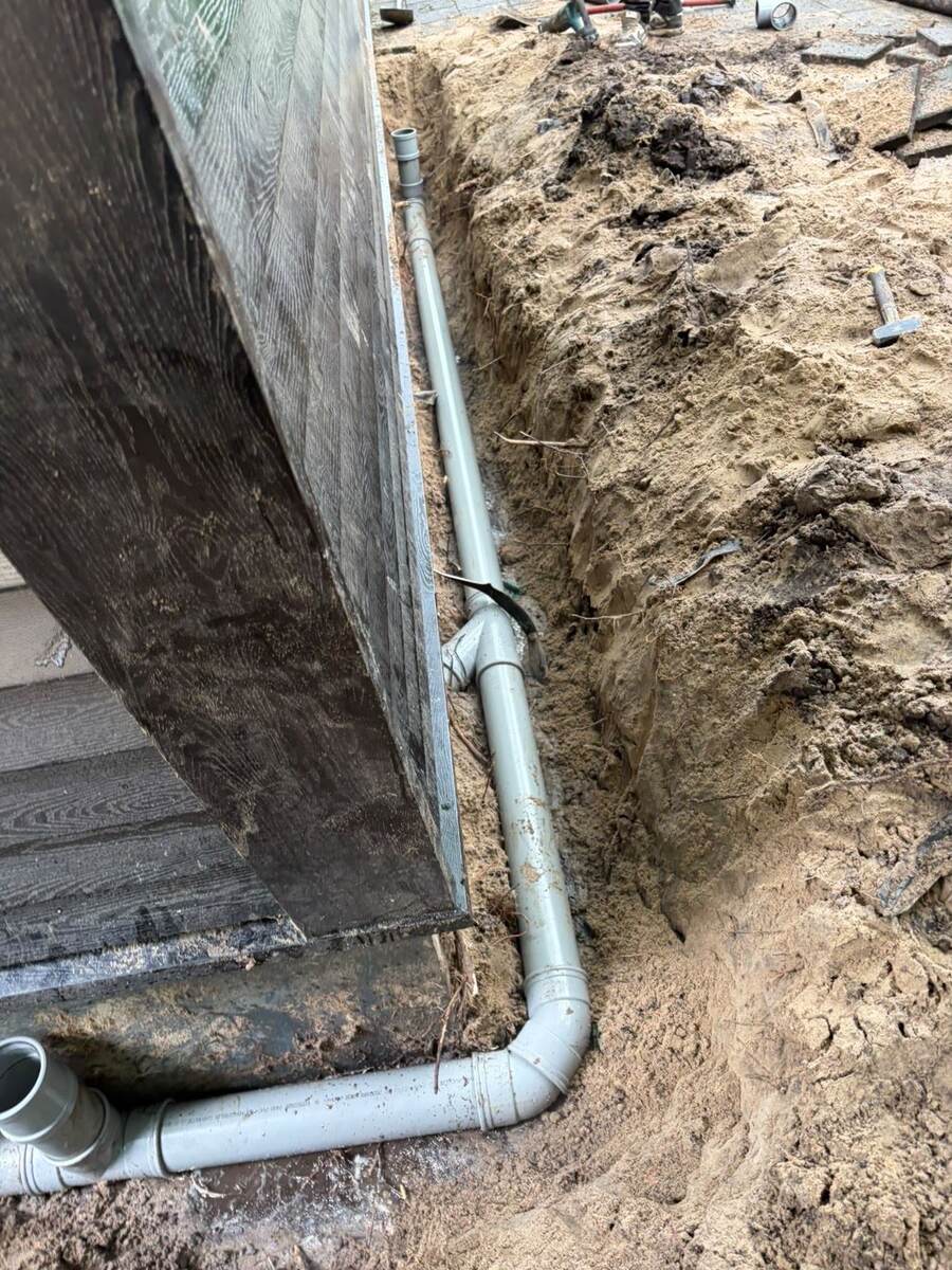Nieuwe pvc-buitenriolering met bochten in een open sleuf langs de gevel