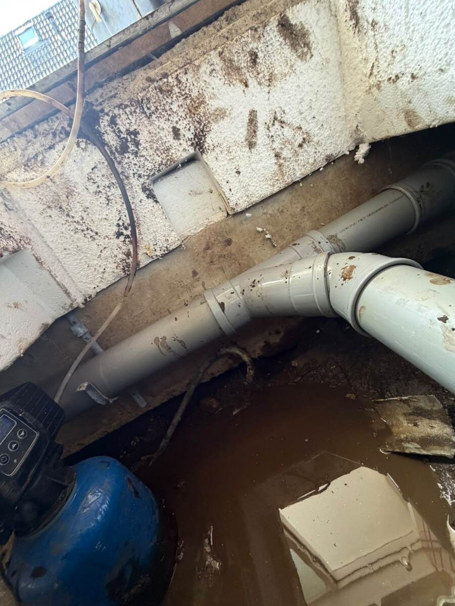 Kruipruimte met water op de bodem, grijze pvc-rioolleidingen en een pompunit