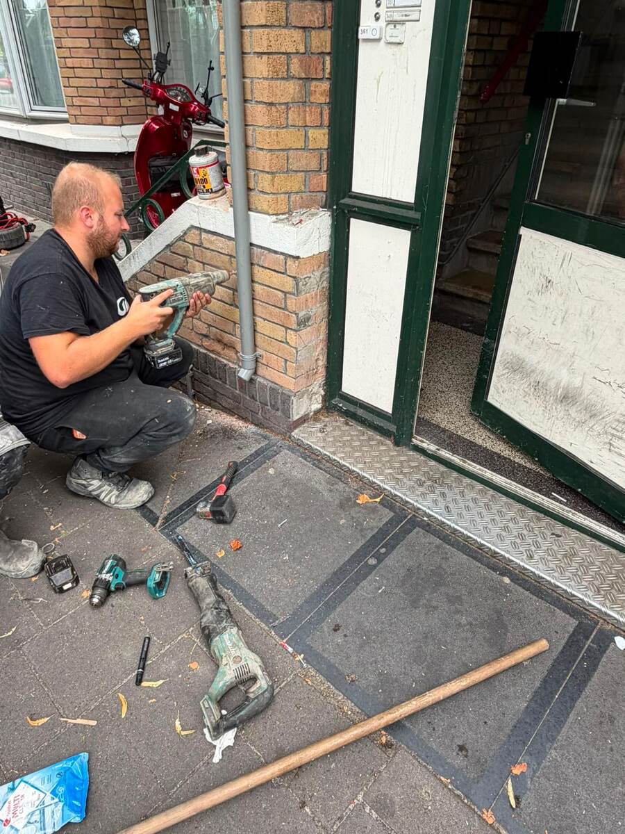 Monteur met accugereedschap bij de opengemaakte stoep voor een voordeur