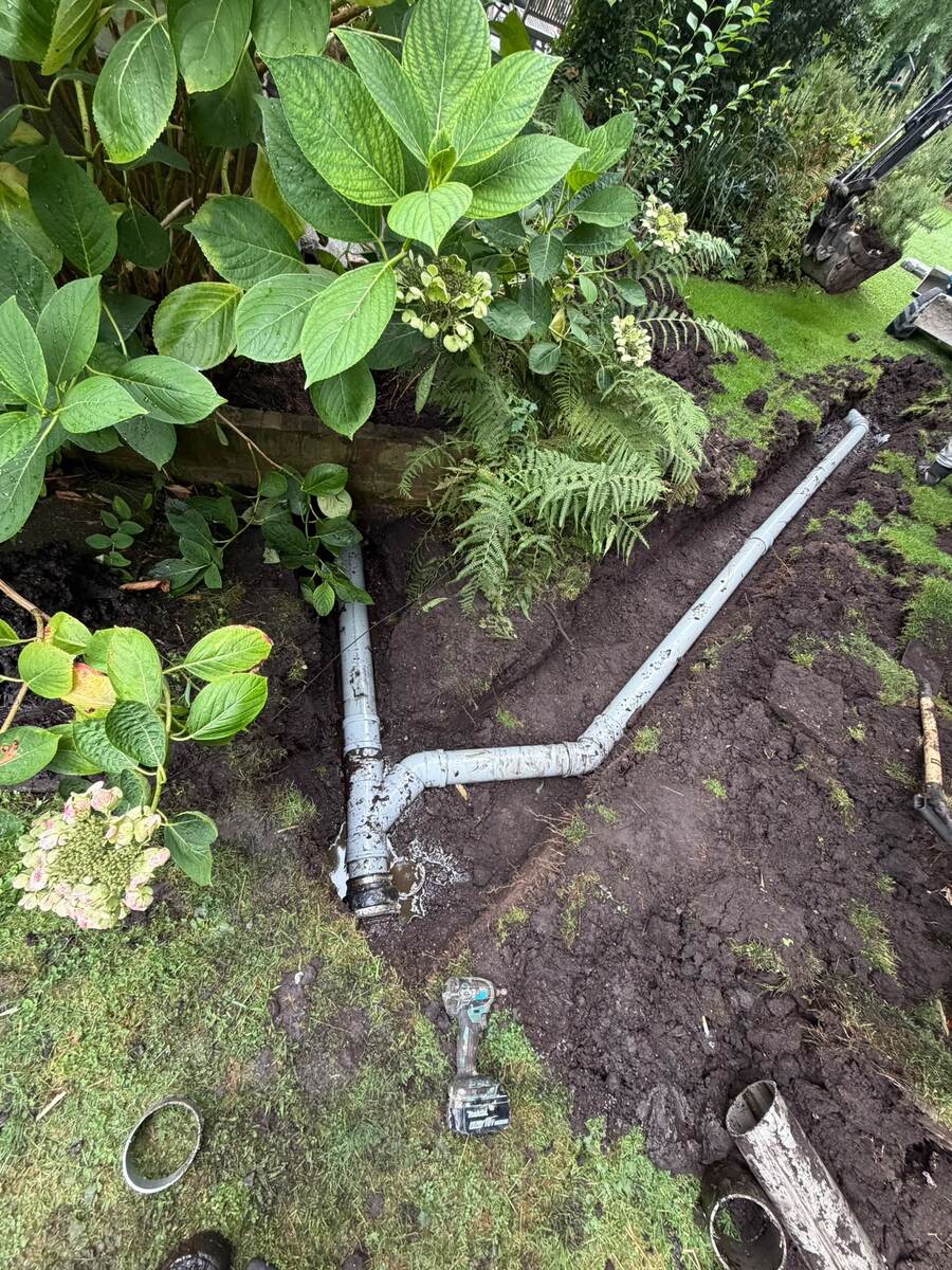 Nieuwe rioolleiding met koppelingen in een sleuf door de tuin tussen de planten