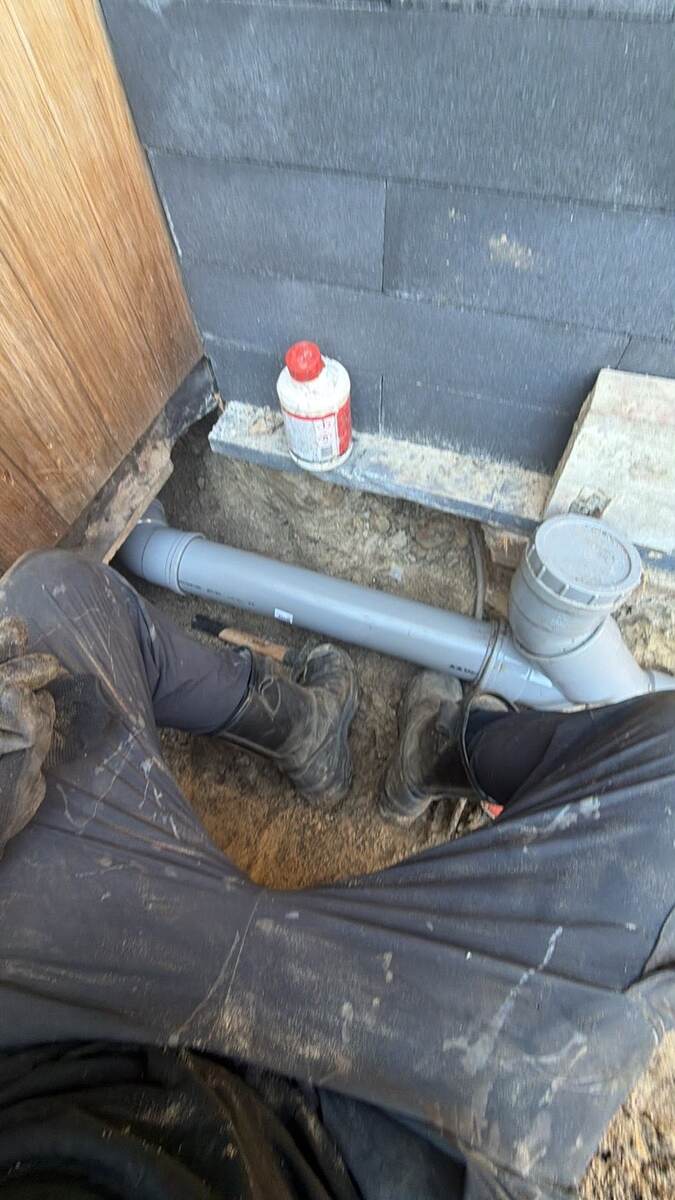Nieuwe pvc-rioolbuis met ontstoppingsstuk in een uitgegraven sleuf naast een woning