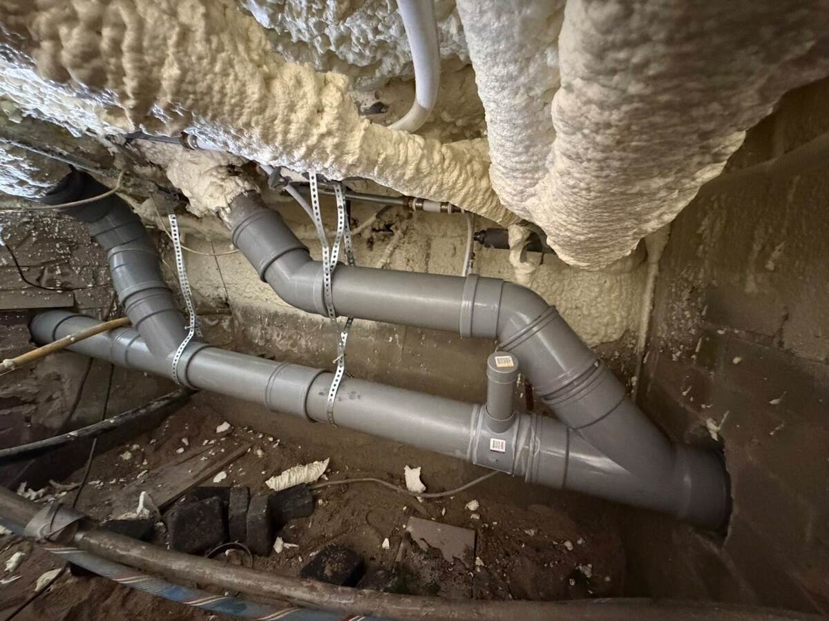 Nieuwe pvc-riolering met ontstoppingsstukken onder een geïsoleerde vloer in de kruipruimte