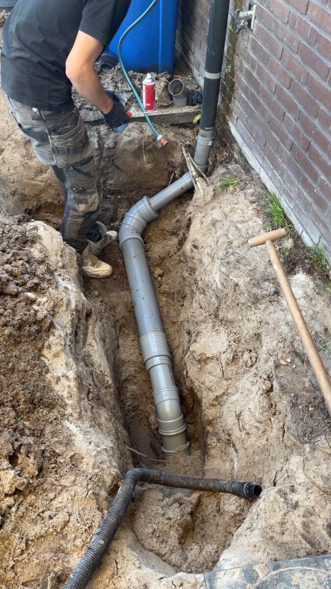 Monteur van Rioolspecialist Hoofddorp vervangt een rioolbuis in een sleuf langs de woning