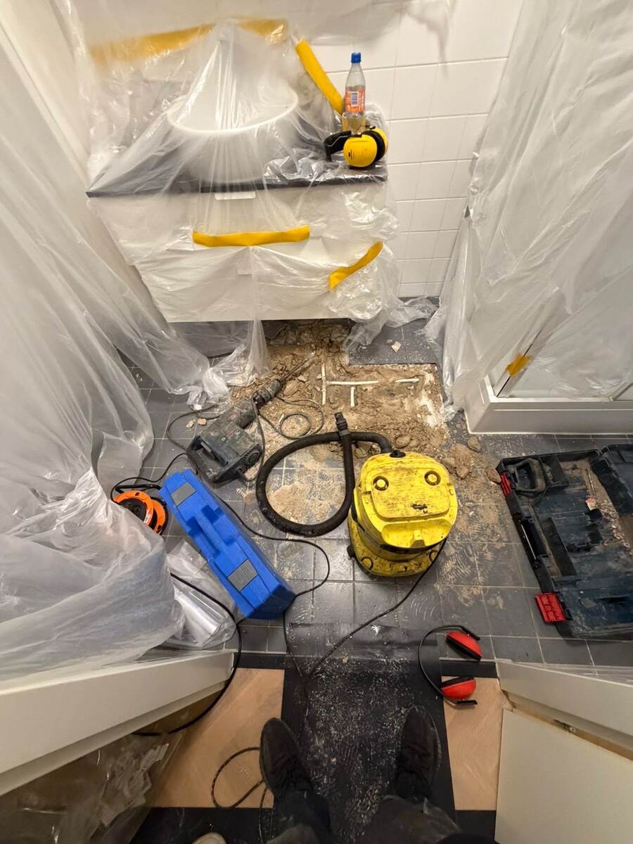 Toiletruimte afgedekt met plastic, met ontstoppingsmachine en gereedschap op de opengemaakte vloer